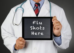 Closeup of a doctor holding a tablet computer with a chalkboard screen with the words Flu Shots Here.